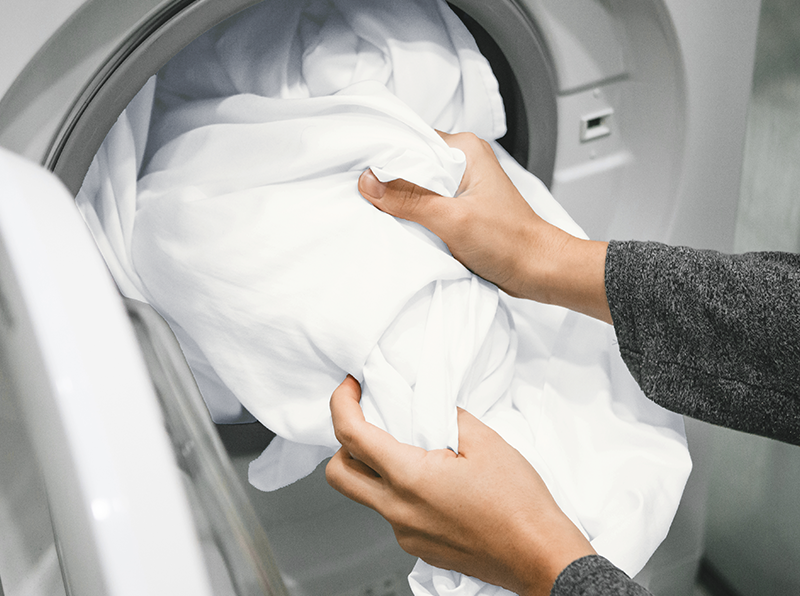 Handen die zachte witte lakens in een wasmachine stoppen, benadrukt eenvoudig onderhoud en machinewasbaarheid.