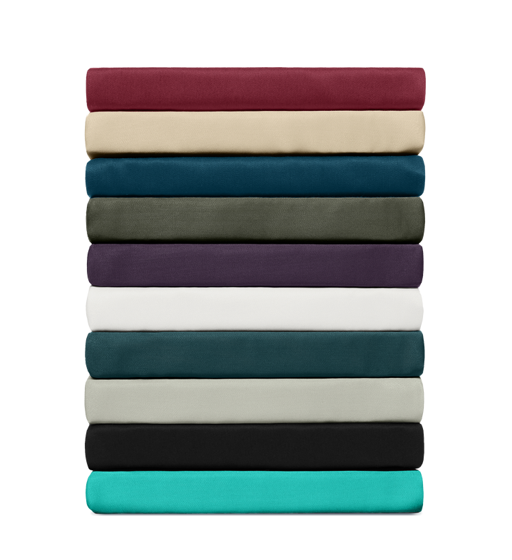 Stapel hoeslakens in diverse effen kleuren, netjes gevouwen en gerangschikt om kleurvariatie en stofkwaliteit te tonen.